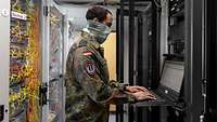 Ein Soldat arbeitet an einem Rechner in einem Netzwerkraum.