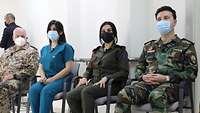 Zwei Frauen und zwei Soldaten mit Mund-Nasen-Schutz sitzen nebeneinander auf Stühlen