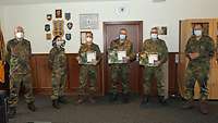 Soldaten stehen nebeneinander in einem Dienstzimmer. Drei davon halten Urkunden in den Händen