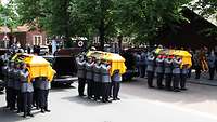 Soldaten tragen bei einer Trauerfeier drei Särge, die mit der Bundesdienstflagge bedeckte sind