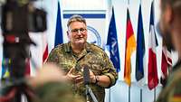 A soldier is standing in front of national flags and speaks into a microphone