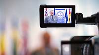 The display of a video camera shows a soldier standing in front of national flags