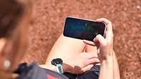 A woman looks at her smart phone. The monitor shows a progress diagram.