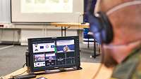 A soldier wearing headphones looks at a monitor