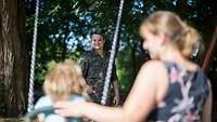 Ein Soldat schubst seine Tochter und Frau auf der Schaukel an.