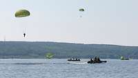 Zwei Fallschirmspringer landen im Schwielowsee, zwei befinden sich noch in der Luft. Mehrere Schnellboote sind auf dem See
