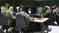 Soldaten in grüner Uniform sitzen in einem Raum an mehreren Computern.