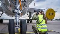 Miriam Altfelder kniet auf dem Boden und fotografiert von oben nach unten das Fahrwerk eines Flugzeuges.