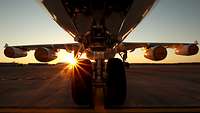 Ein Flugzeug steht auf der Landebahn und im Hintergrund geht die Sonne auf.