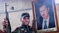 Soldat der syrischen Regierungstruppen posiert mit Portrait von Präsident Bashar al Assad.