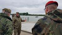 Ein rumänischer, ein britischer und ein deutscher Soldat stehen am Ufer eines Flusses und sprechen miteinander.
