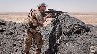 Ein Soldat mit blauer VN-Mütze steht mit seinem Gewehr im Anschlag hinter einem Lavasteinfelsen in der Wüste 