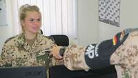 Eine Soldatin übergibt mehrere Reisepässe an einen Soldaten mit MP-Armbinde
