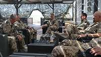 Eine Soldatin sitzt mit fünf weiteren Kameraden auf einer Sitzgruppe im Außenbereich der Betreuungseinrichtung