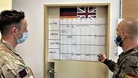 Two soldiers with German and with British uniform are talking on a blackboard on a door.