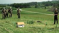 Mehrere Soldaten stehen auf einer Wiese vor einem Modell des umliegenden Geländes.