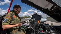 Ein Soldat im Cockpit schaut die Gurte des Schleudersitzes an.