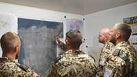 Sechs Soldaten stehen vor einer Lagekarte, einer weist mit einen Zeigestab auf einen Punkt der Karte 