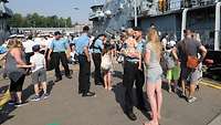 Marinesoldaten in blauer Arbeitsuniform und Zivilisten, vor allem Kinder und Frauen, stehen gemeinsam auf einer Hafenpier.