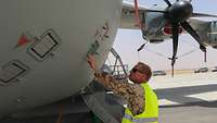 Ein Soldat steht neben dem Airbus A400M und kontrolliert den zuvor erfolgten Einbau der Scheinzielmunition im Flugzeug