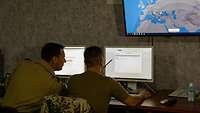 Zwei Soldaten sitzen vor einem Computer und sehen sich Flugbewegungen an.