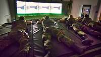 Vier Soldaten liegen mit je einem Sturmgewehr G36 auf einer Matte vor dem Simulator