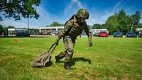 Ein Soldat zieht mit seiner rechten Hand eine schwere Tasche über eine Rasenfläche