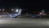 Zwei A400M stehen nachts auf einem Flugplatz.