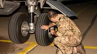 Ein Soldat kniet neben den Reifen eines A400M und untersucht den Reifen.
