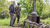 Ein General und ein Zivilist stehen neben einer Mauer, in die ein Stahlgehäuse mit einem kuppelartigen Dach eingesetzt ist..