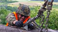 Ein Soldat verzurrt bei der Bahnverladung eine Kette. Er trägt einen Gefechtshelm und eine orangfarbene Warnweste.