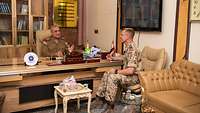 Zwei Soldaten sitzen in einem Büro in Ledersesseln und unterhalten sich. Im Hintergrund steht ein Holzschrank mit Büchern