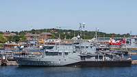 A small grey warship berthed at a pier.