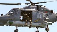 A service member in battle dress aboard an airborne helicopter.