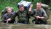 Drei Soldaten durchqueren gemeinsam einen Wasserlauf.