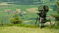 Ein Radarsystem mit Radarschüssel steht auf einem Berg, darunter erstreckt sich grüne Landschaft.