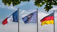 Die Fahnen Deutschlands, Frankreichs und des Eurocorps wehen an Fahnenmasten im Wind.