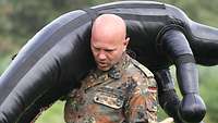 Ein Soldat beißt die Zähne zusammen und schleppt eine 50 Kilo schwere Puppe über den Platz.