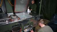 Zwei Soldaten arbeiten an einer Feldküche. Einer kniet davor und überprüft die Temperatur des Kochers