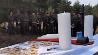 Im Vordergrund ein Altartuch mit Kerzen und Keksen auf einer Motorhaube, im Hintergrund Soldaten mit Liedertexten