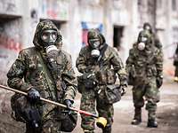 Fünf Soldaten in ABC-Schutzkleidung gehen hintereinander durch ein Fabrikgelände