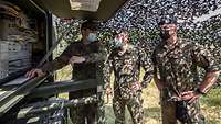 Drei Soldaten mit Mund-Nasenschutz stehen neben einer „Satellitenkommunikation Bodenstation dynamisch".