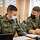 Zwei Soldaten mit Mund-Nasenschutz sitzen an einem Schreibtisch und besprechen sich.