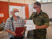 Ein Soldat mit Unterlagen in der Hand steht neben einem älteren Mann und spricht mit ihm