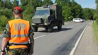 Ein Militärpolizist sperrt die Straße für eine deutsche Militärkolonne. Ein belgischer Militärpolizist steht an der Straße