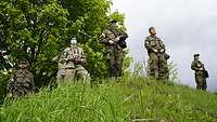 Sechs Soldaten in teilweise unterschiedlichen Uniformen stehen auf einem Hügel und beobachten das Gelände