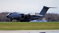 Ein Flugzeug vom Typ A400M landet auf einem Rollfeld. Die Reifen qualmen beim Aufsetzen.