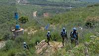 Vier Soldaten sind auf Patrouille und steigen einen Berg hinauf. Sie tragen blaue Helme und Westen