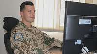 Ein Soldat sitzt an einem Schreibtisch und schaut auf den Computermonitor vor sich