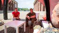 Eine Sportlerin, eine Soldatin und ein Soldat sitzen an einem Tisch 